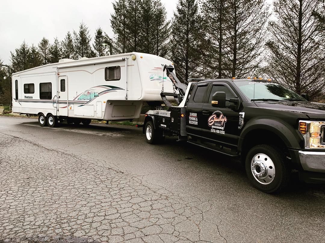Tow truck towing a large white and blue RV on a paved road.