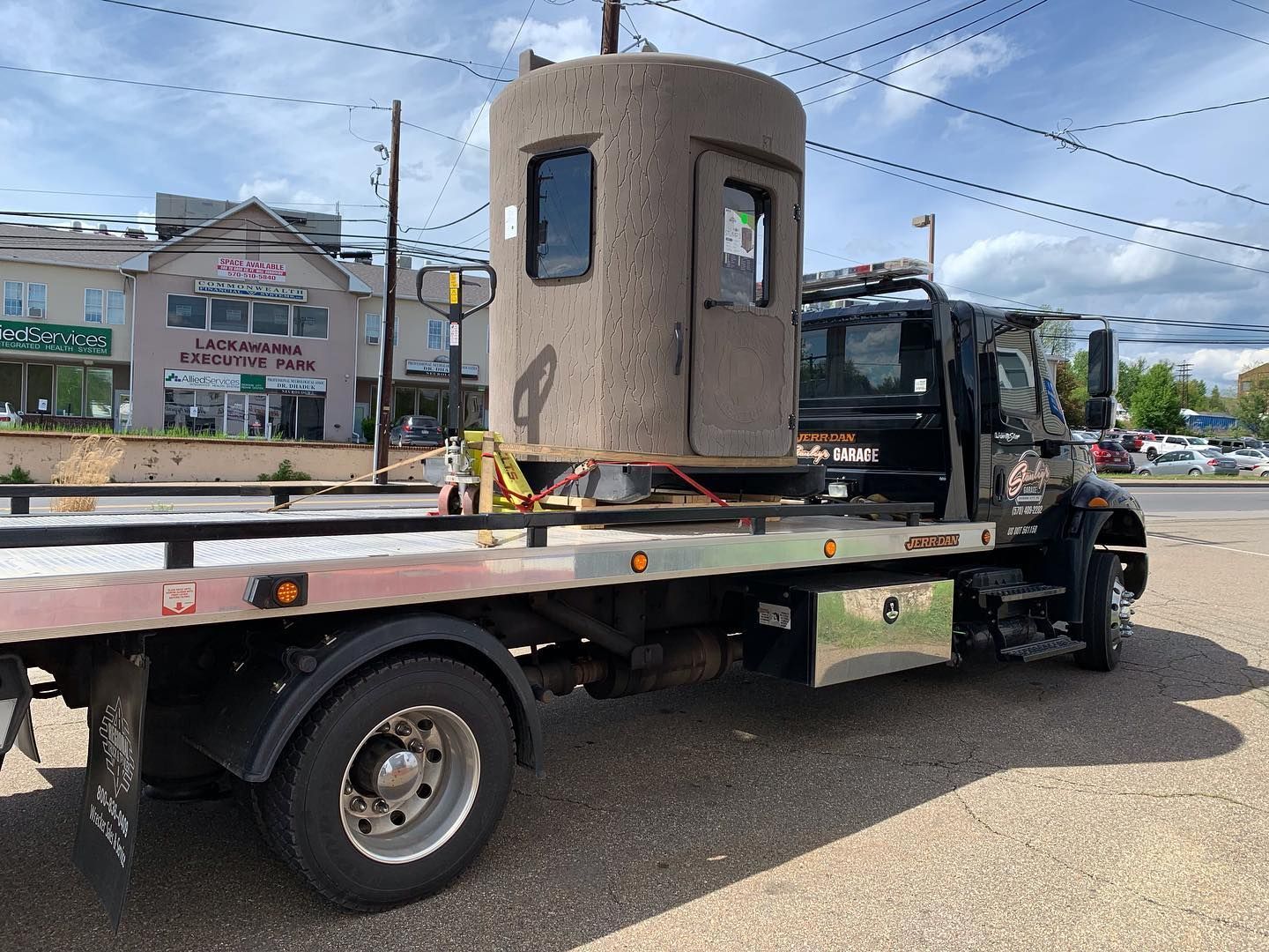A large cylindrical structure, possibly a guard booth, is being transported on a flatbed tow truck.