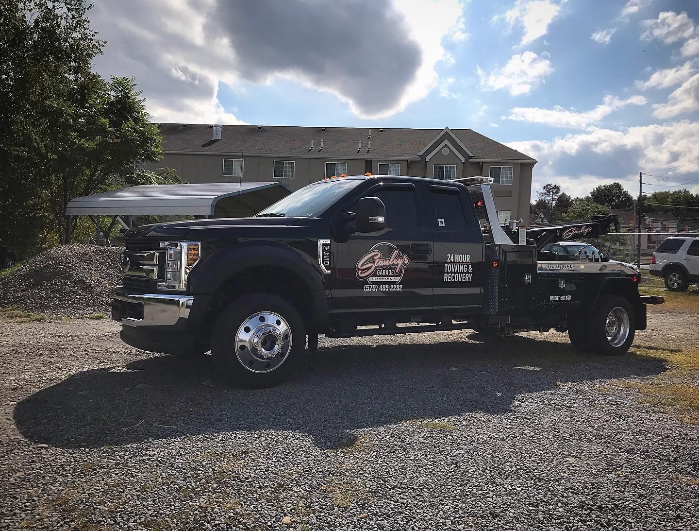 Black tow truck parked on gravel in front of a building on a sunny day.