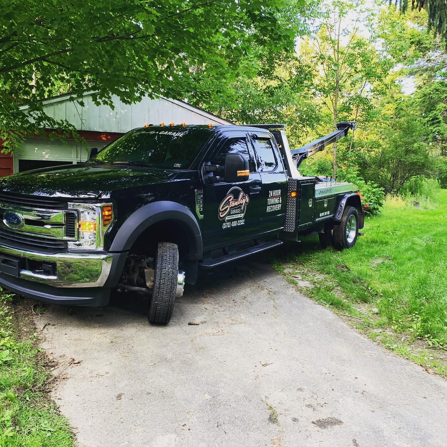 Black tow truck parked on a driveway next to a grassy area.