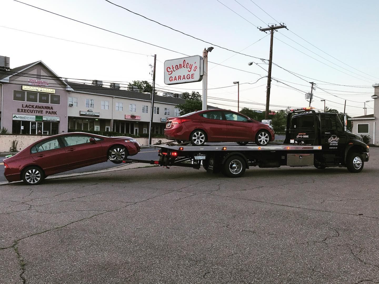 Tow truck carrying two red cars, in front of 