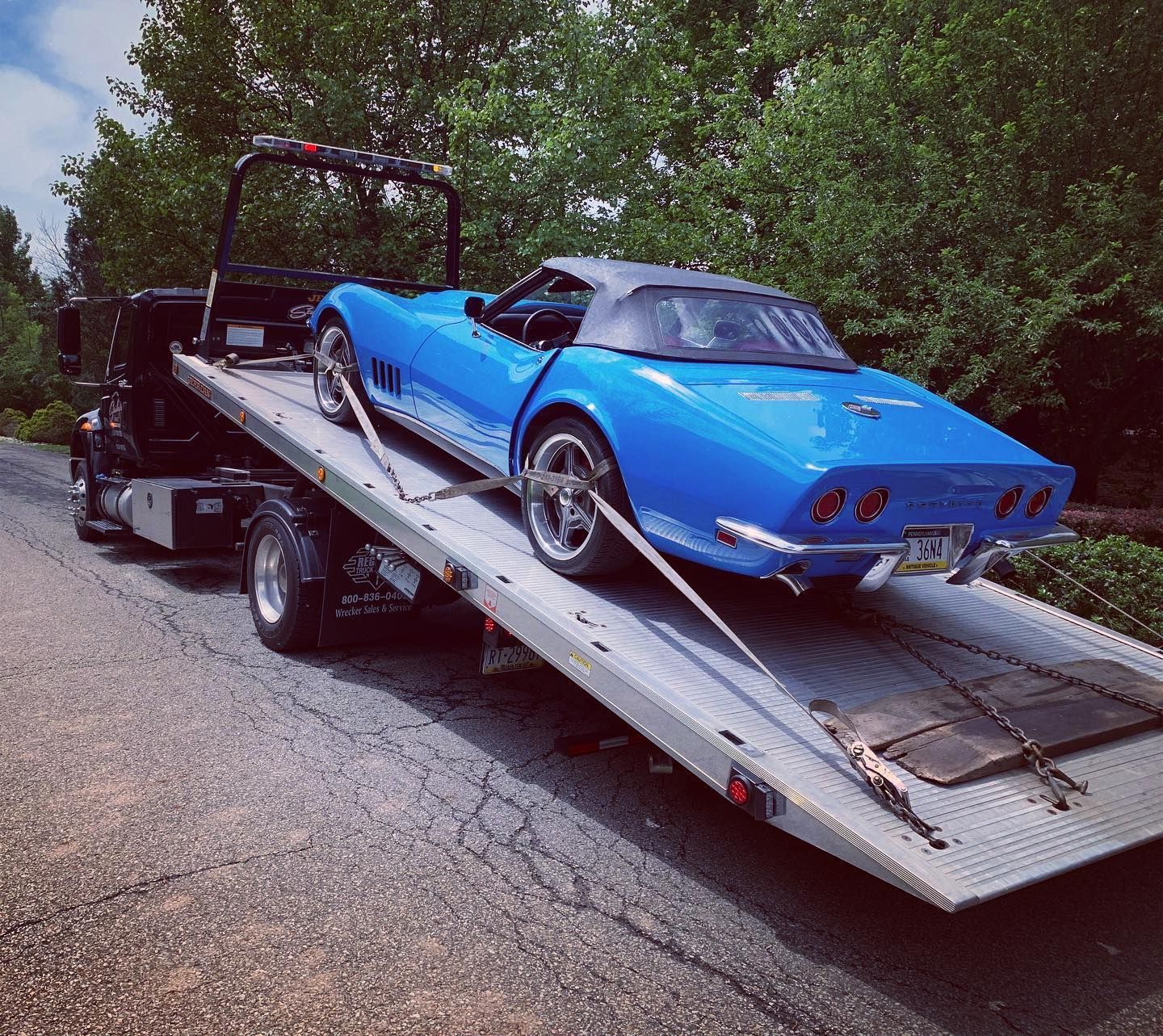 Blue classic Corvette convertible on a tow truck, being transported on a road.