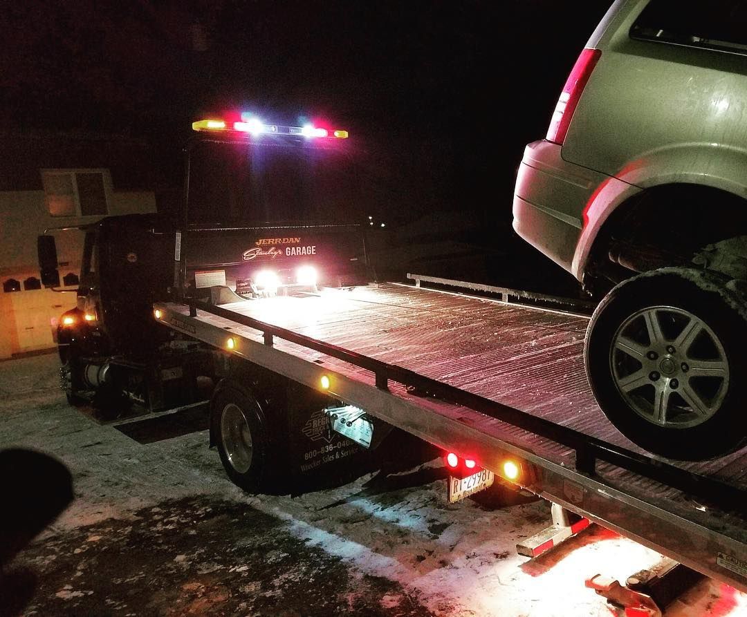 Tow truck loading a silver SUV at night. Red and white lights are illuminated.