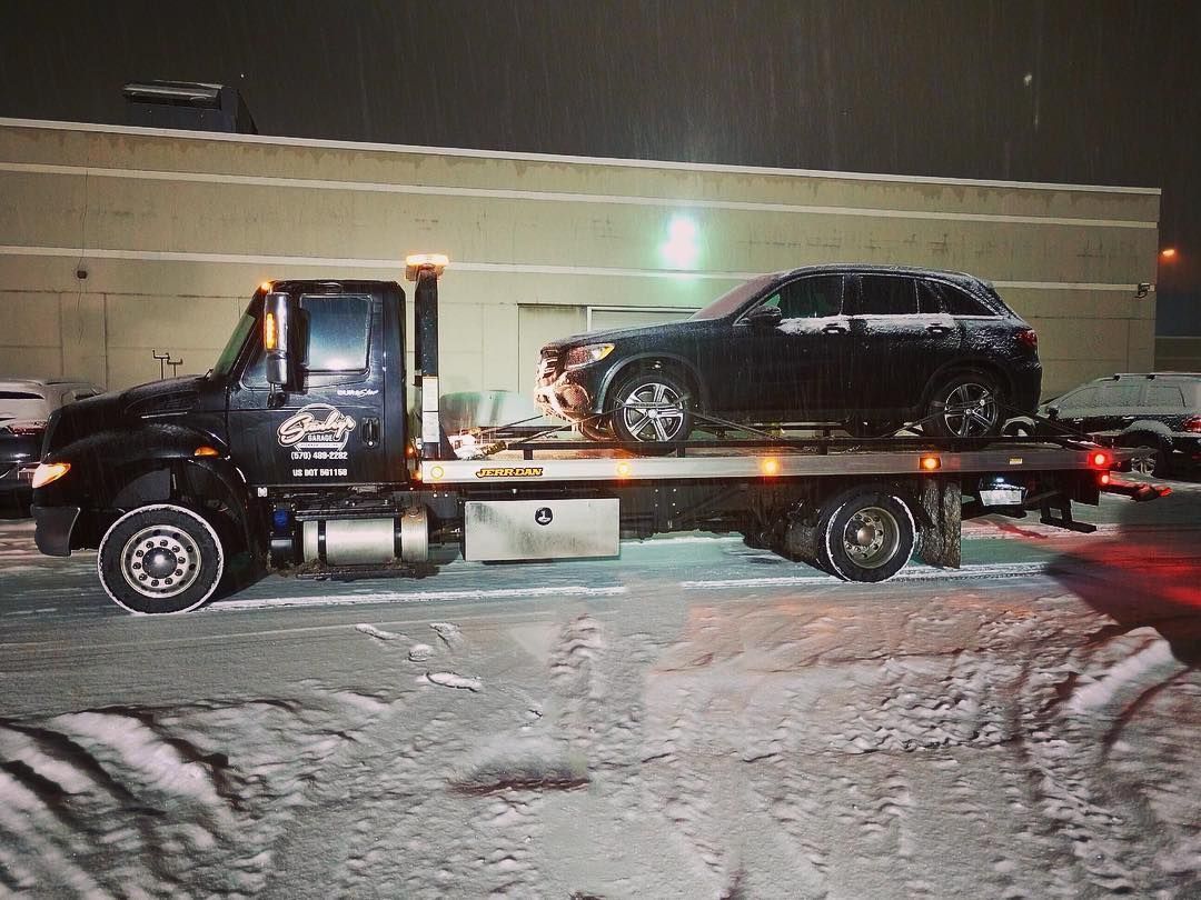 A tow truck loaded with a dark-colored SUV on a snowy night.