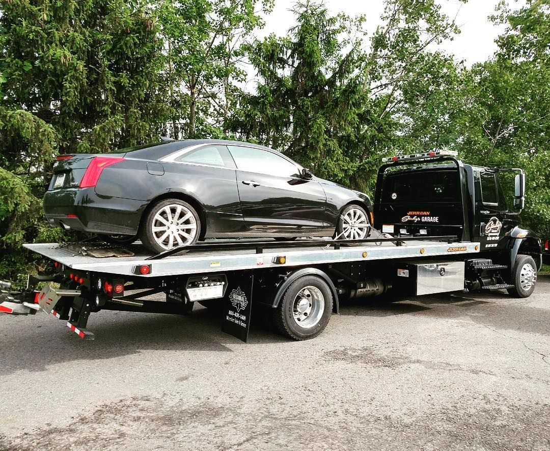 Black car on a flatbed tow truck outdoors near trees.