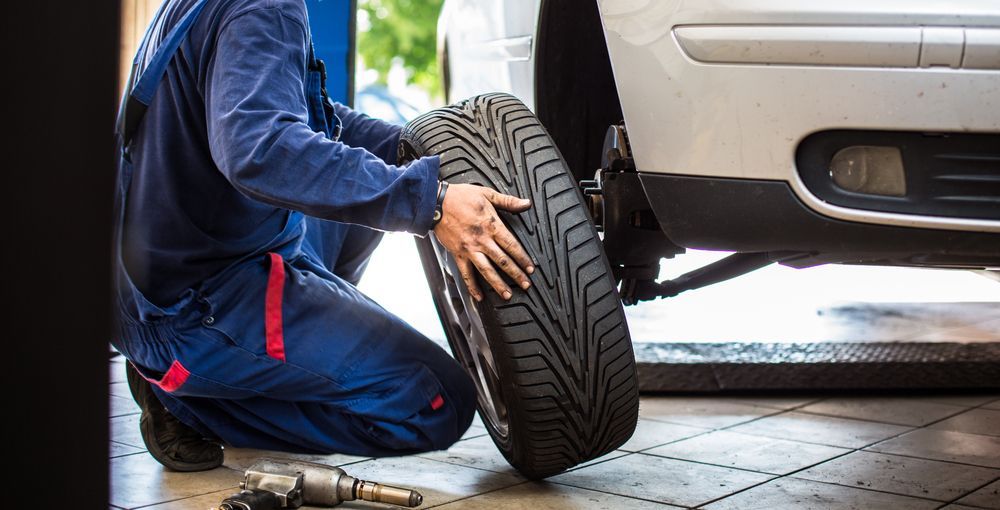 Mechanic in blue overalls changes a tire on a white car in a garage.