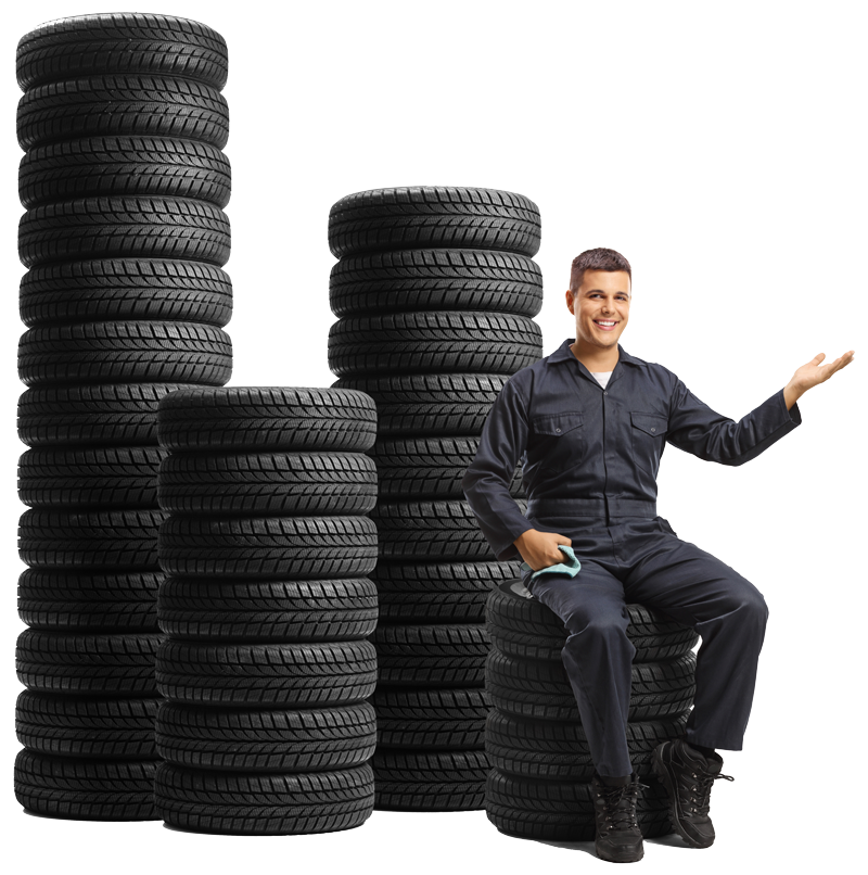 Mechanic sitting on tires next to tire stacks, gesturing, white background.