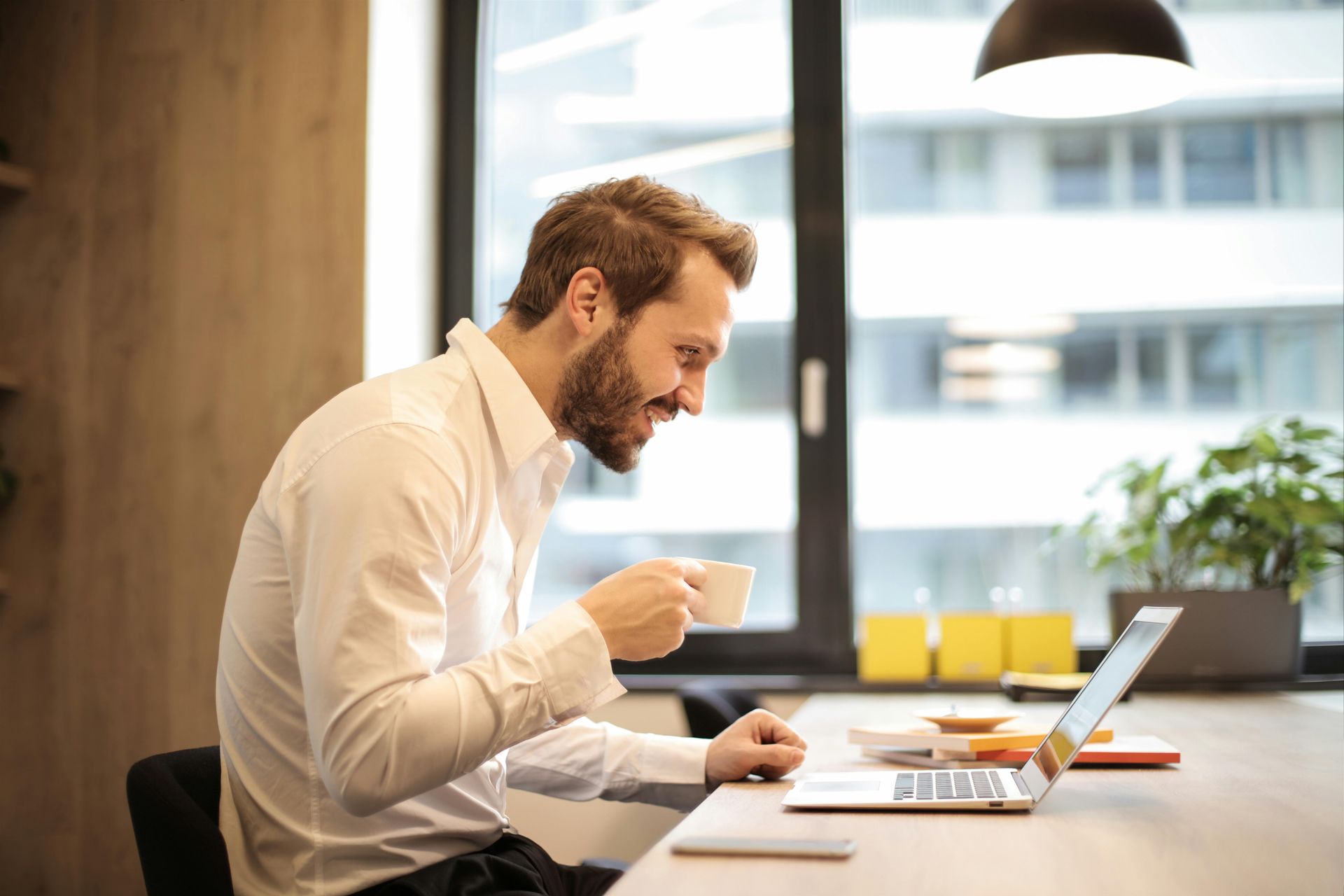 A man is drinking coffee while using a laptop computer.