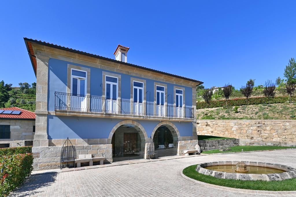 Uma grande casa azul com arcos e uma fonte na frente.