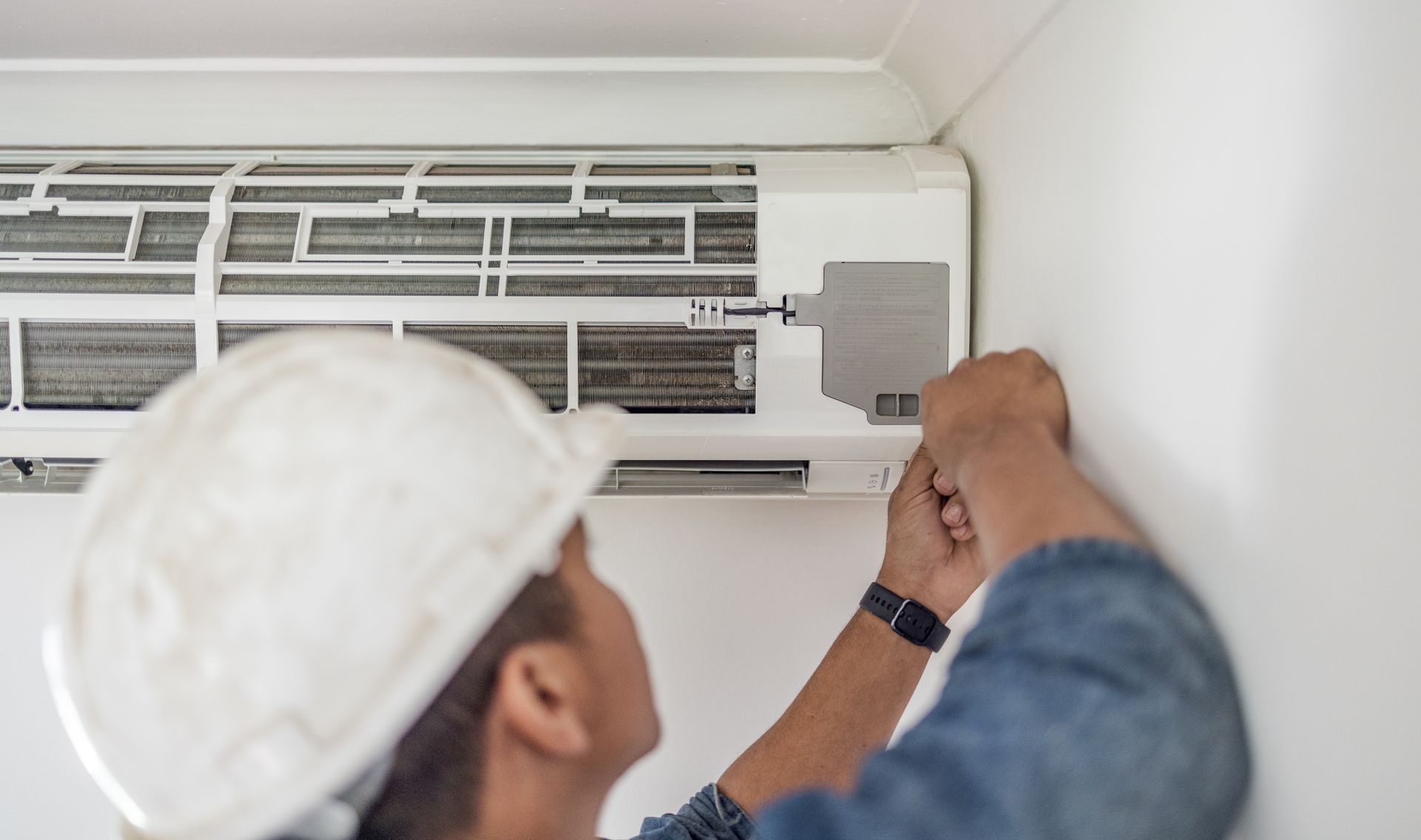 Technician installing or repairing a wall-mounted air conditioning unit.