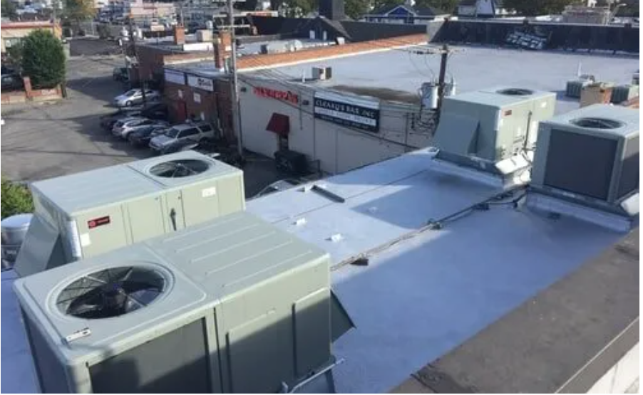 There are a lot of air conditioners on the roof of a building.