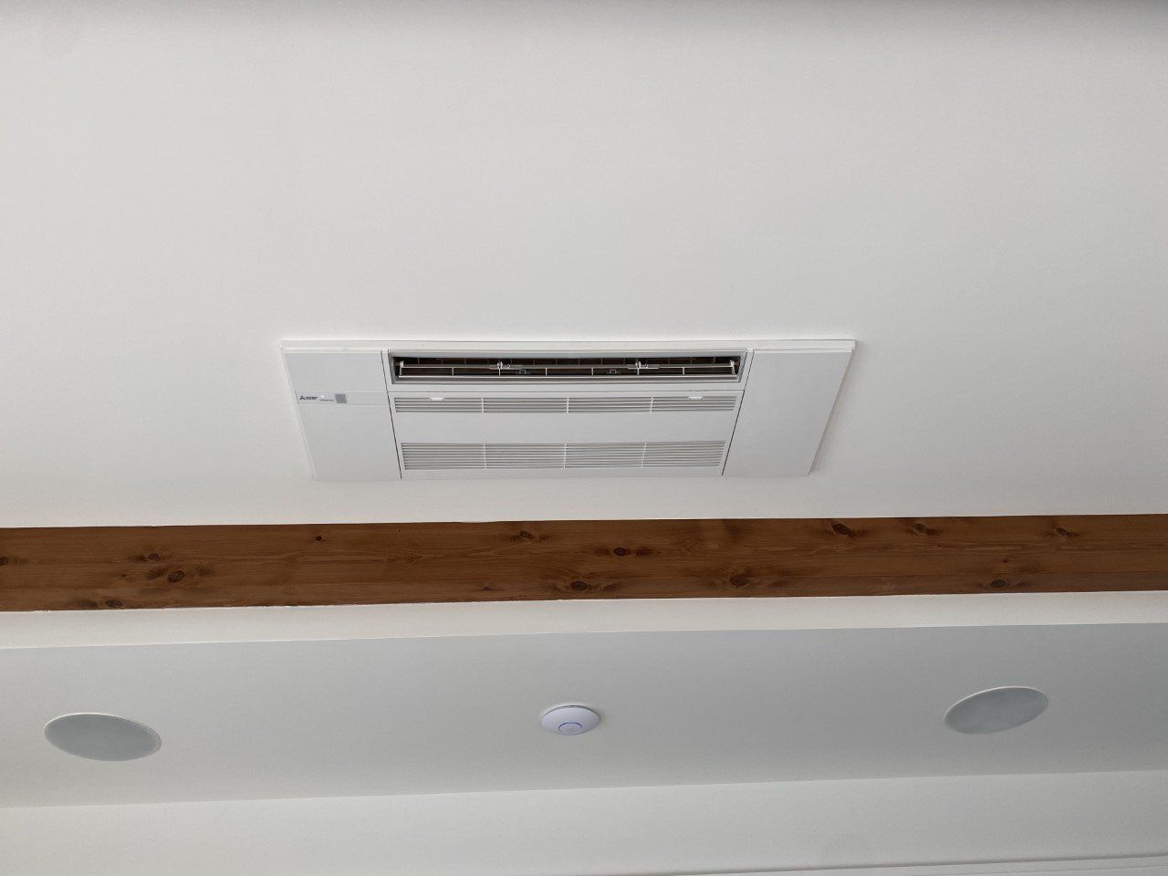A white air conditioner is mounted to the ceiling of a room.