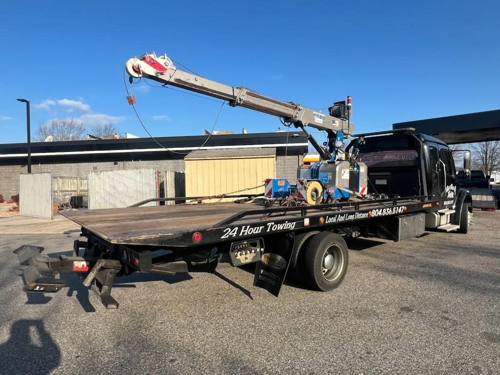 Tow truck with extended crane boom, parked on pavement, sunny day.