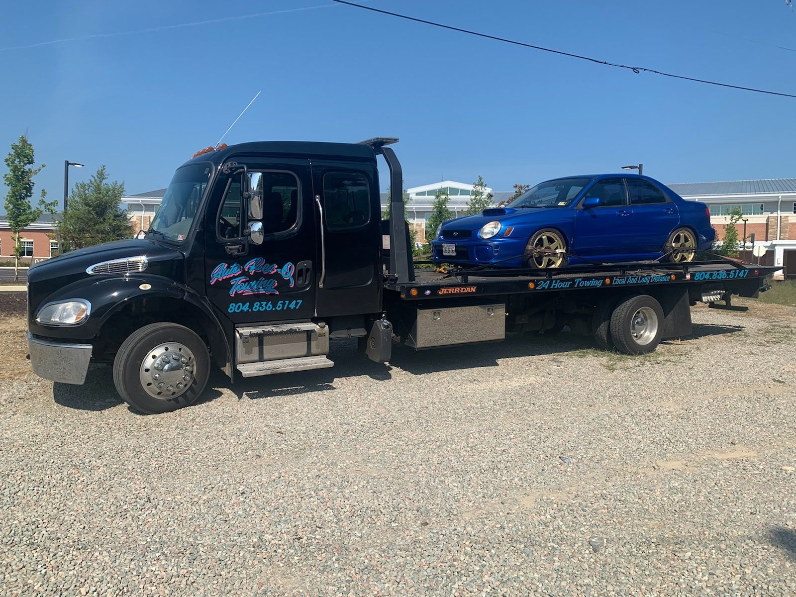 Black tow truck carrying a blue sports car on a sunny day.