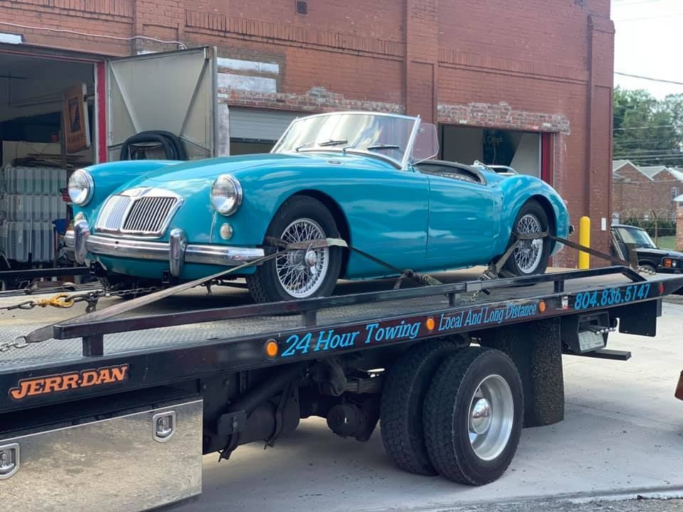 Teal convertible sports car on a tow truck; brick building in background.