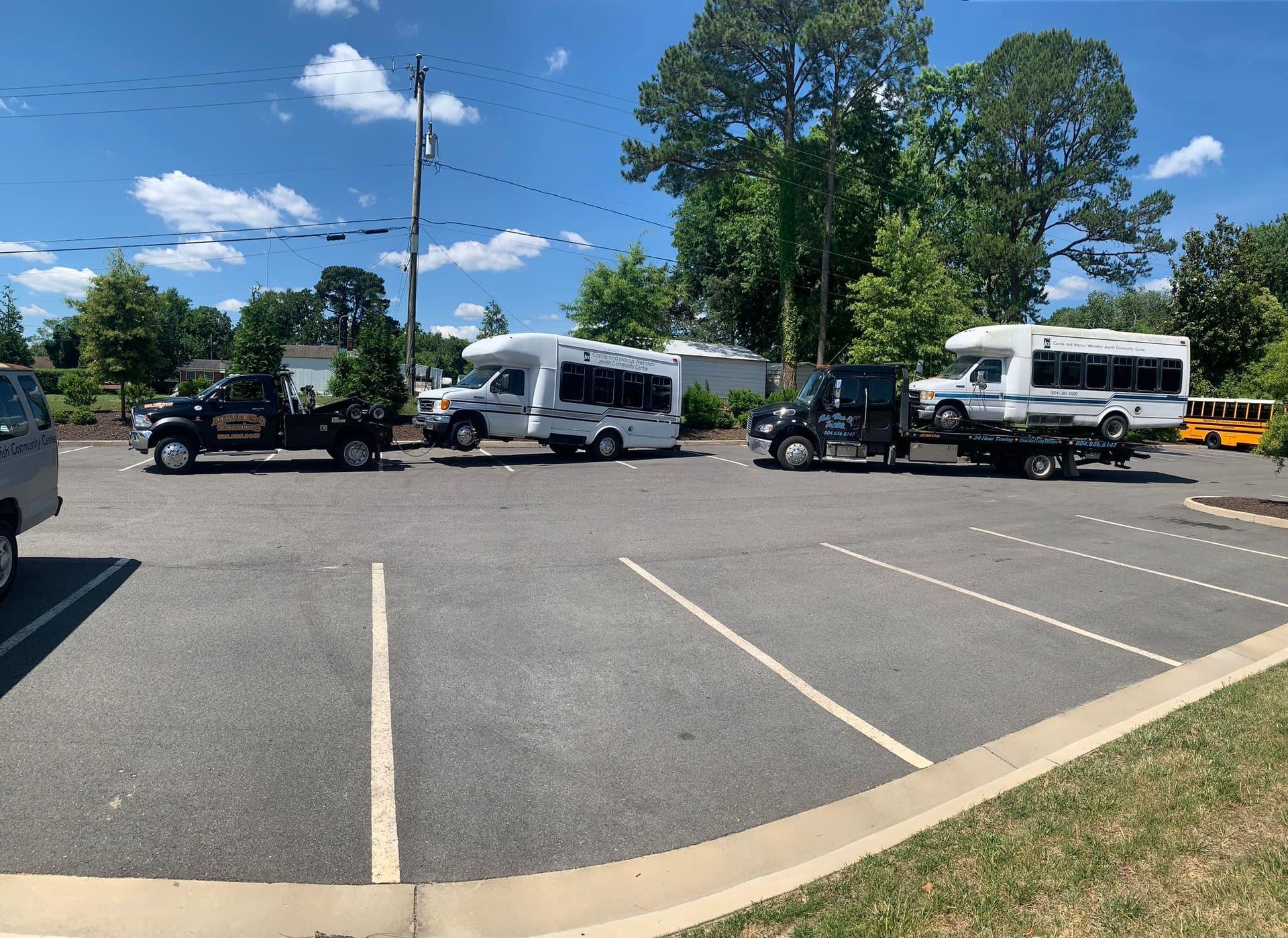 Several vehicles parked in a paved parking lot under a blue sky, including tow trucks, vans, and a motorhome.