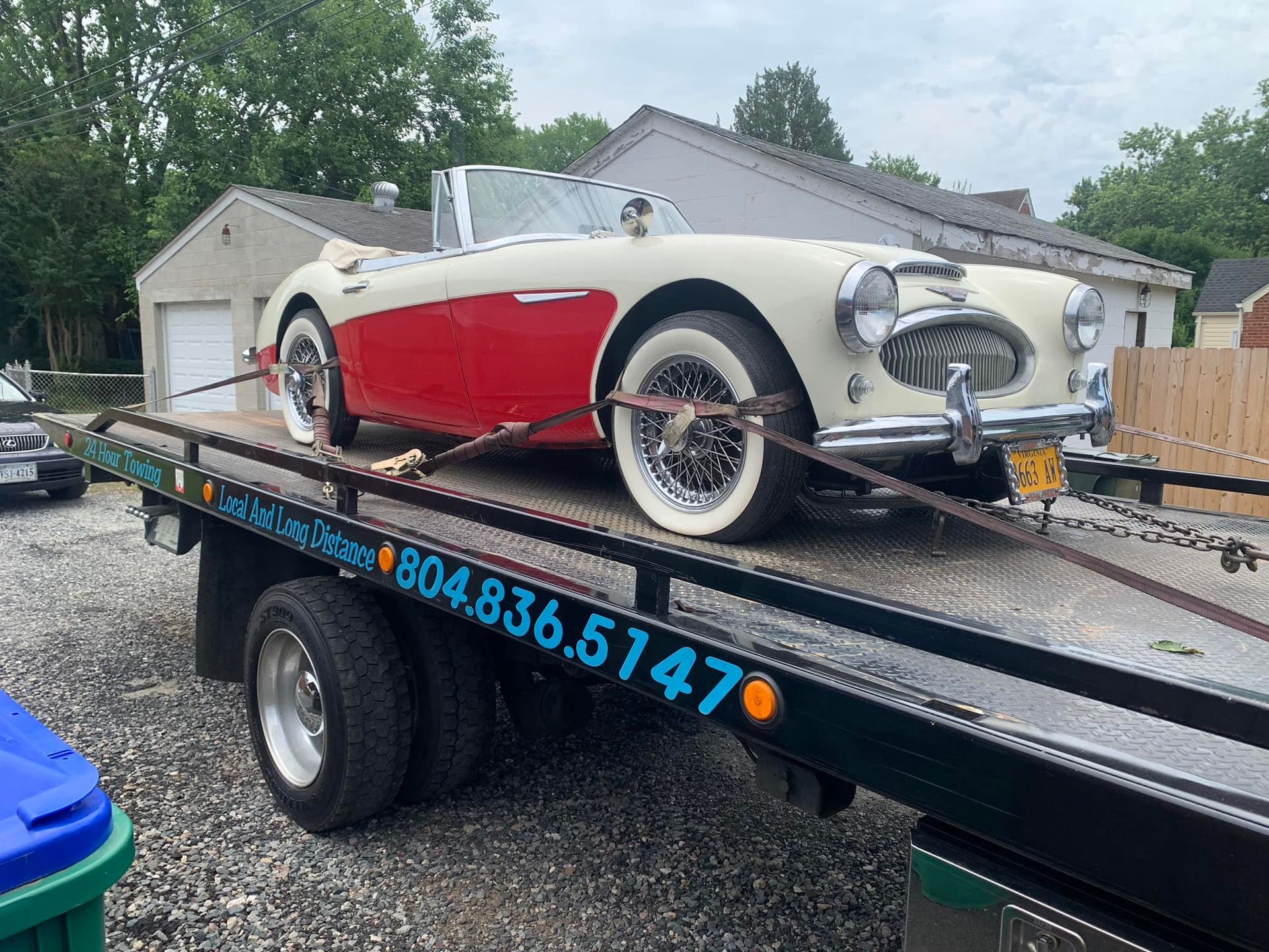 Red and white vintage Austin-Healey convertible on a tow truck, ready for transport.