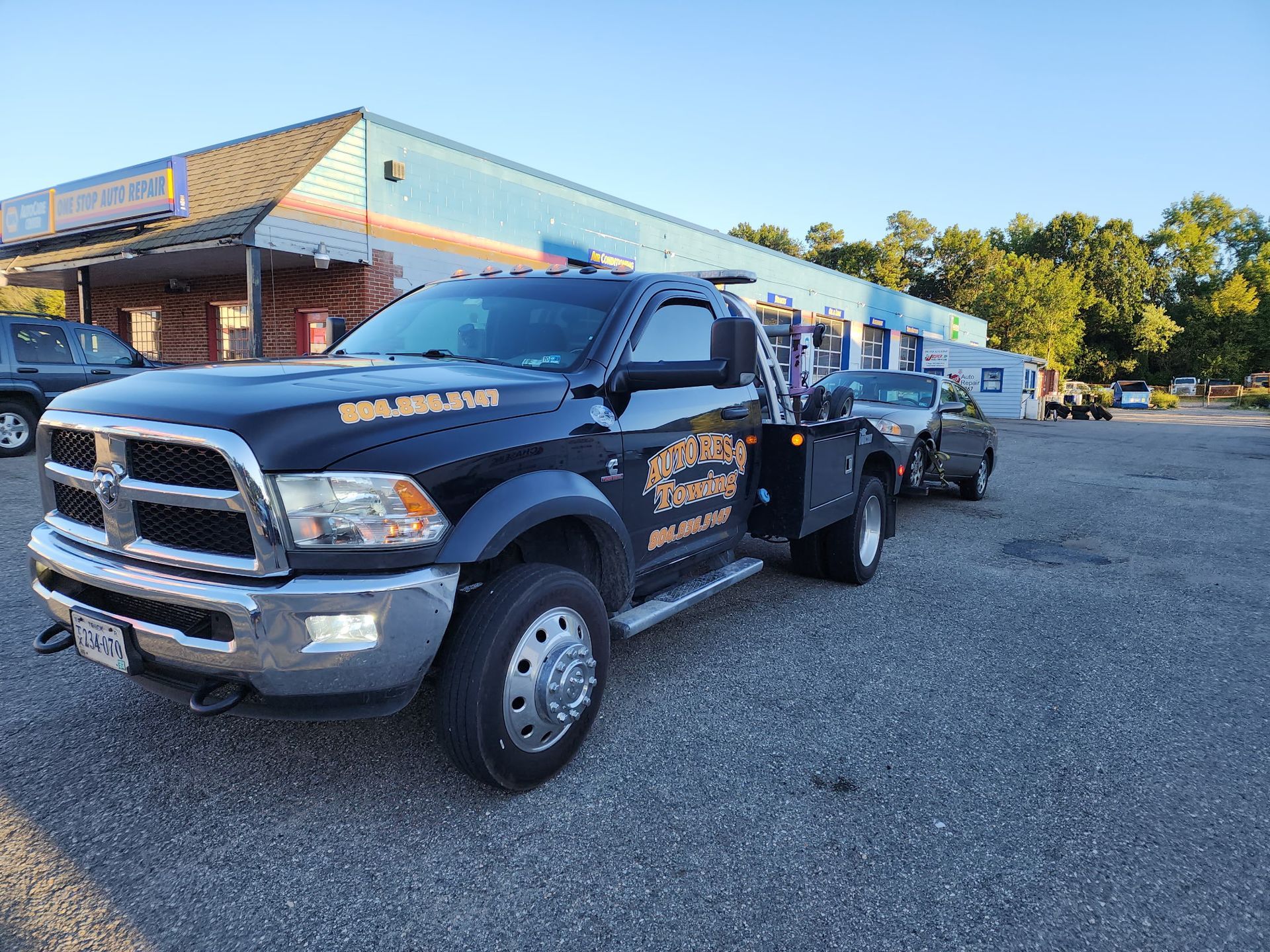 Black tow truck towing a car in a parking lot; building in the background.