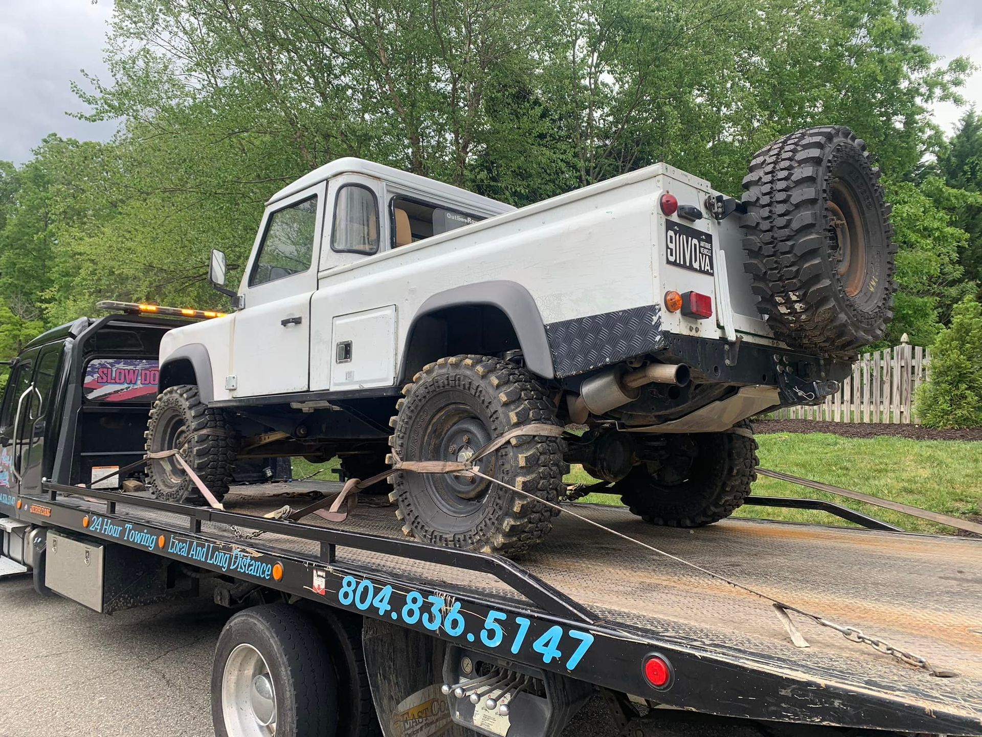 White Land Rover Defender pickup truck on a tow truck, tires secured.