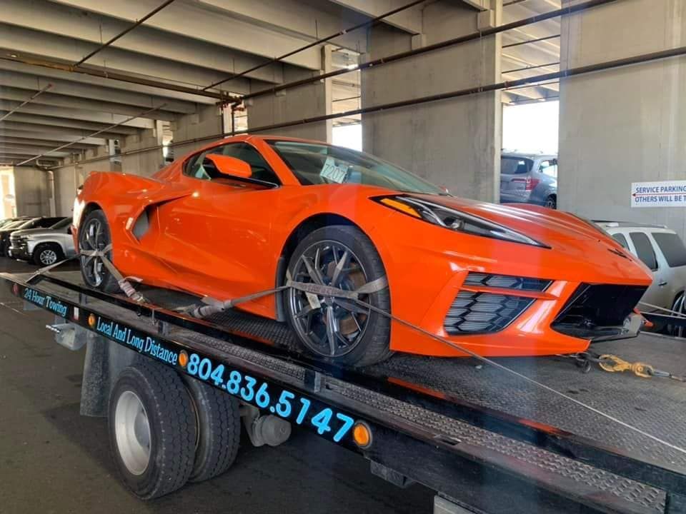 Bright orange Corvette sports car on a flatbed tow truck. The car is strapped down in a covered area.