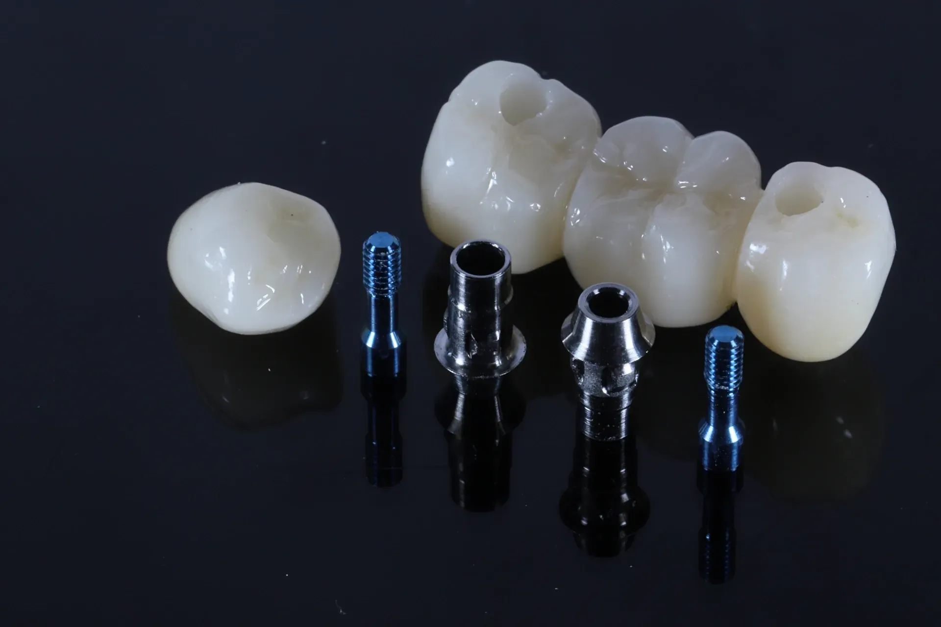 Dental implants with crowns and screws on a dark surface. — AB Esthetic Dental Laboratory in Robina, QLD