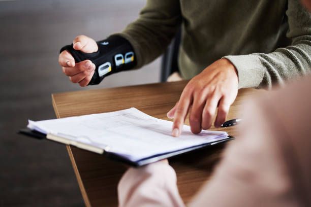 A man wearing a wrist brace is sitting at a table with a clipboard.