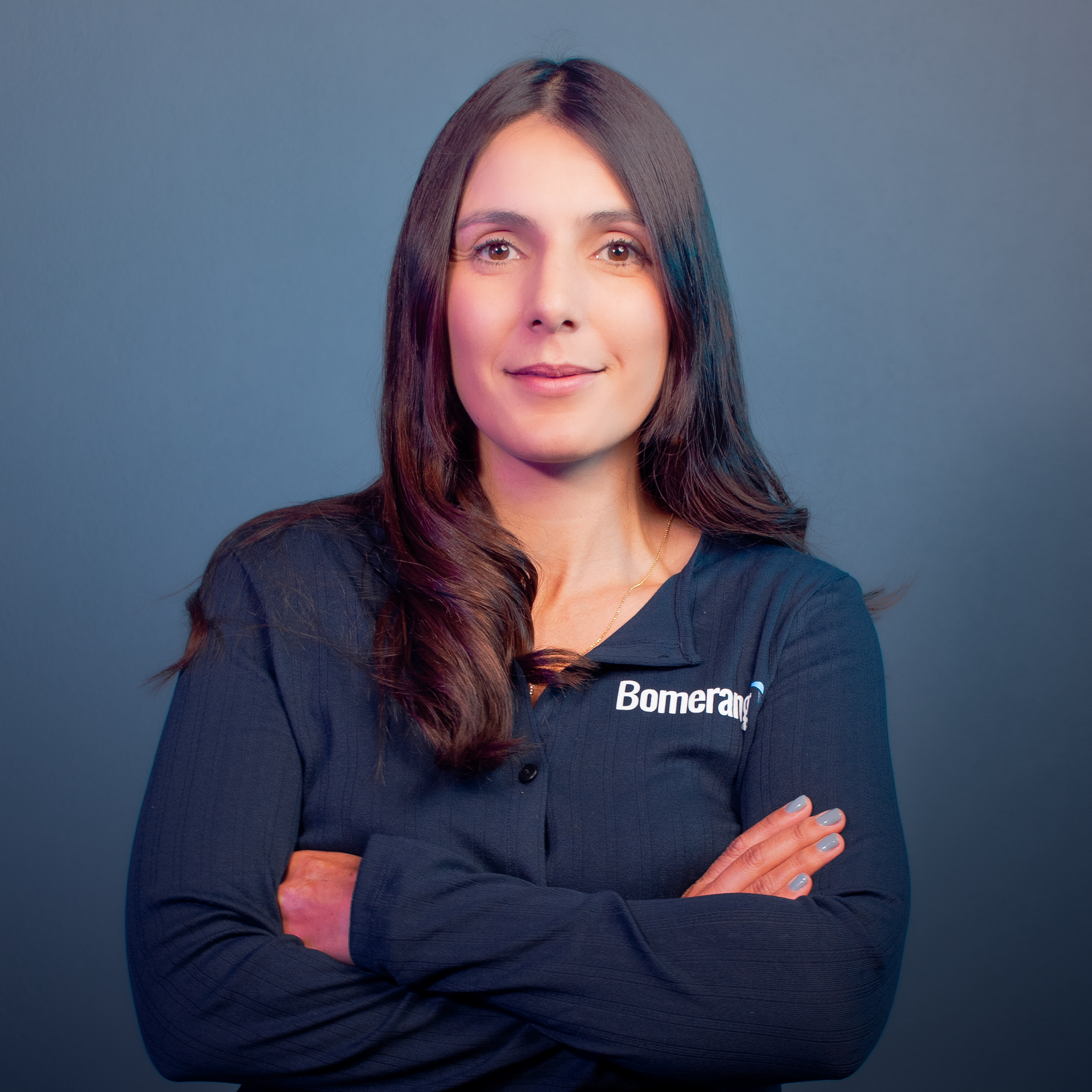 Una mujer está de pie con los brazos cruzados frente a un fondo azul.
