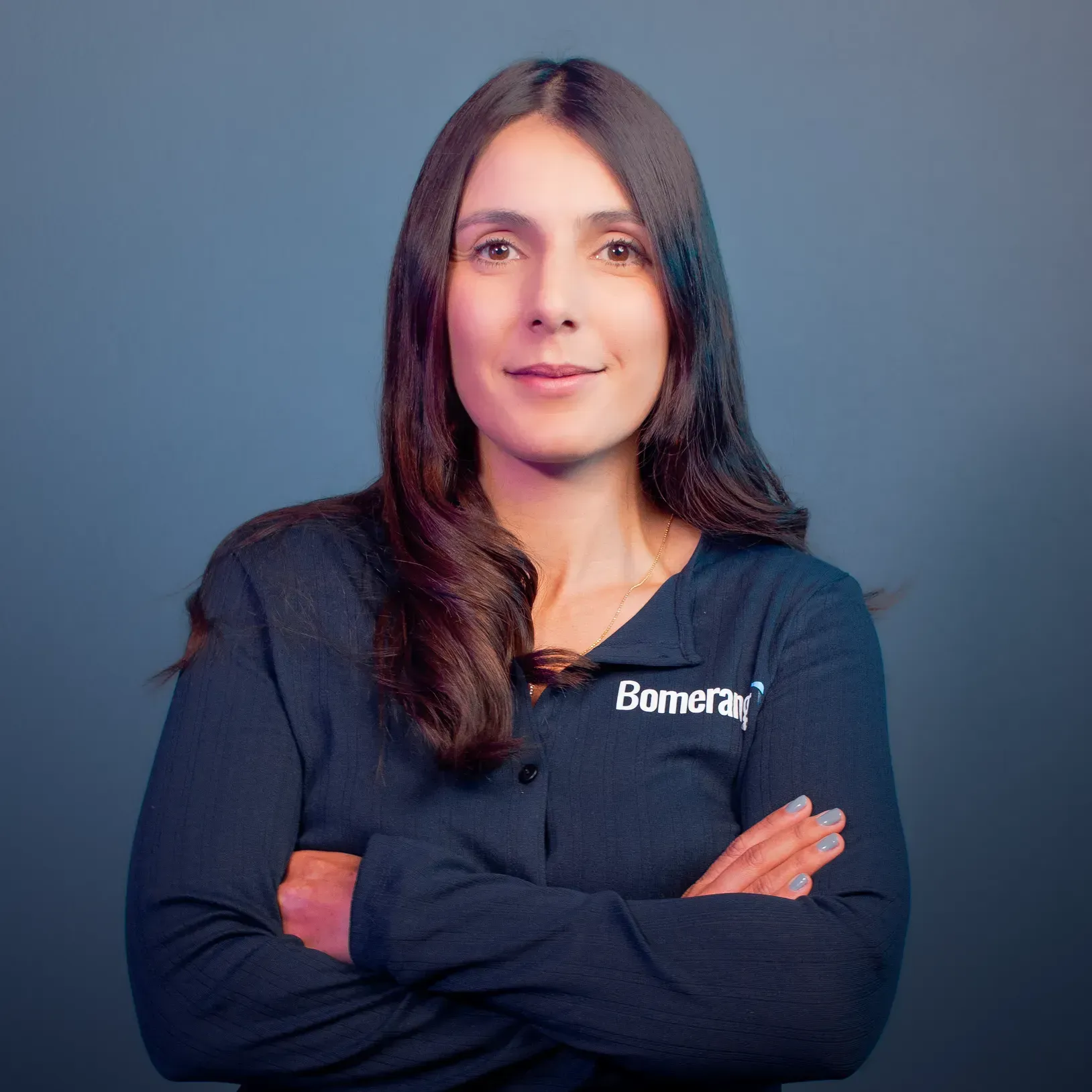 Mujer con cabello largo castaño, vestida con una camisa azul marino, con los brazos cruzados, sonriendo.