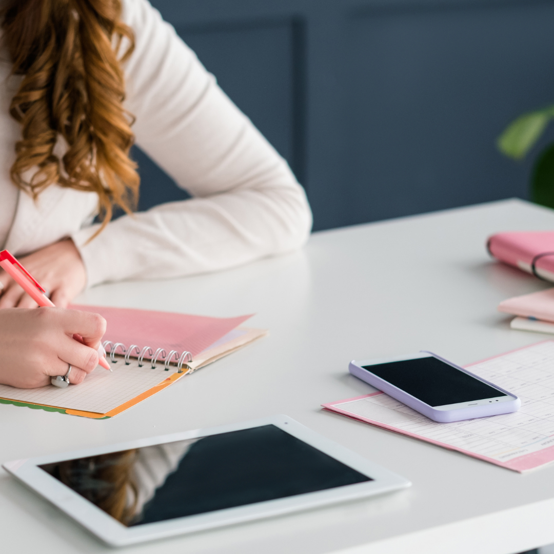 a woman is sitting at a desk writing in a notebook, working on keyword optimization for her business