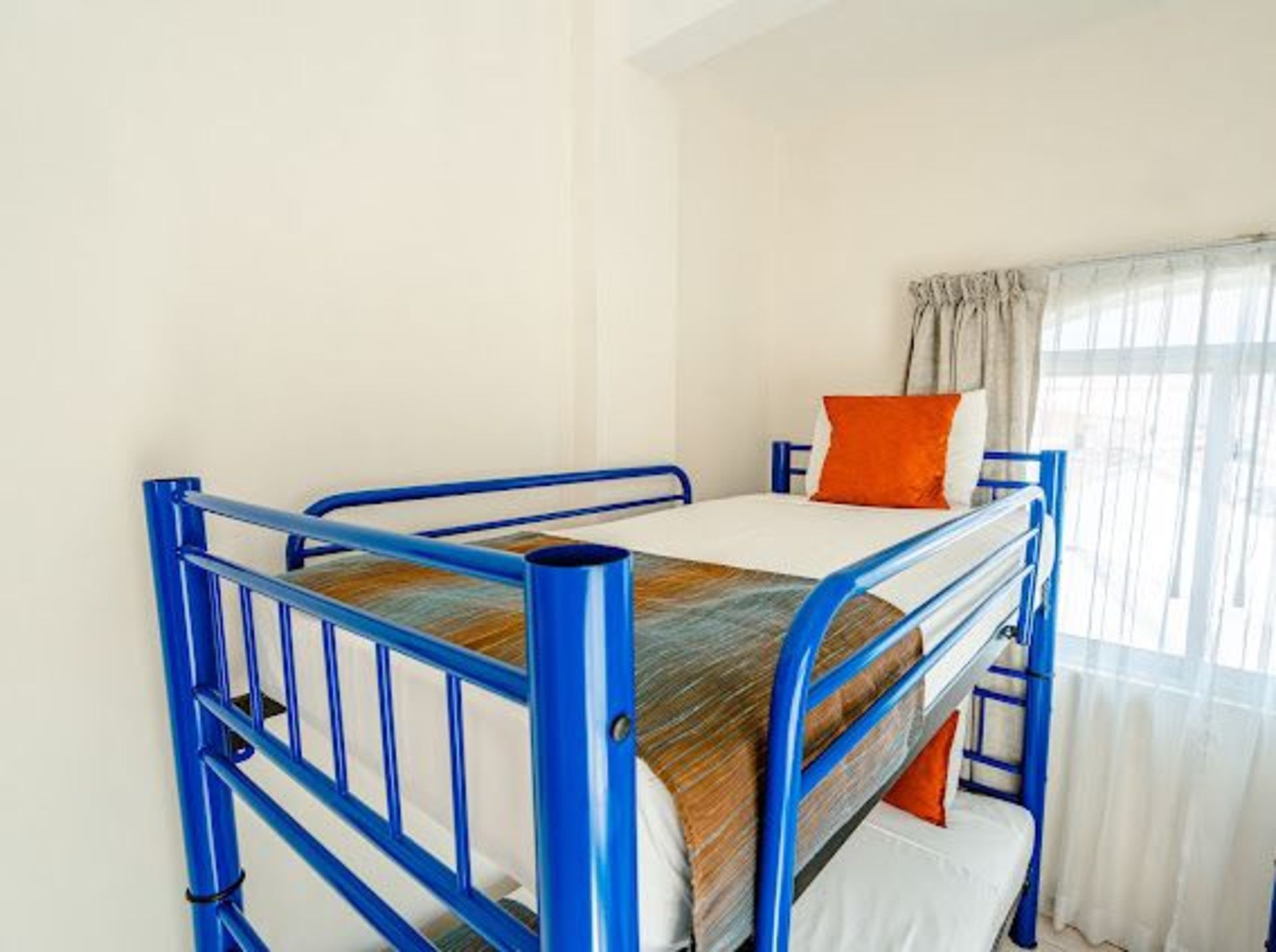 Literas azules en una habitación luminosa con ventana y almohadas naranjas.