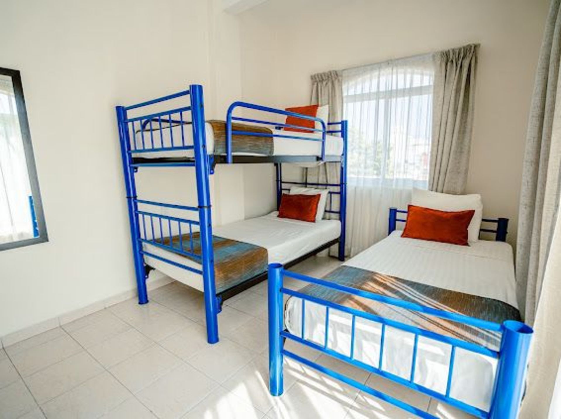 Una habitación con tres camas: dos literas y una cama individual; estructura de metal azul y sábanas blancas.