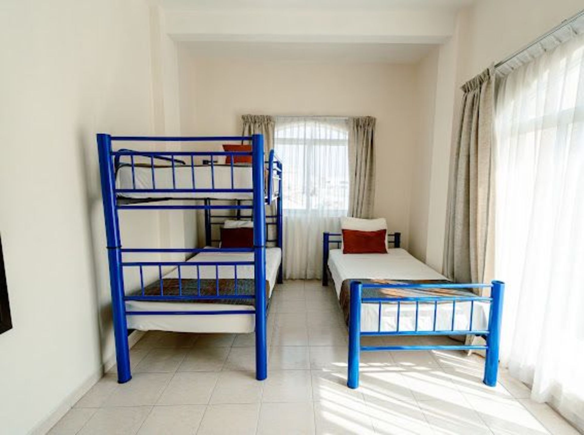 Una habitación compartida con literas azules y una cama individual. Luminosa, con ventana y paredes blancas.