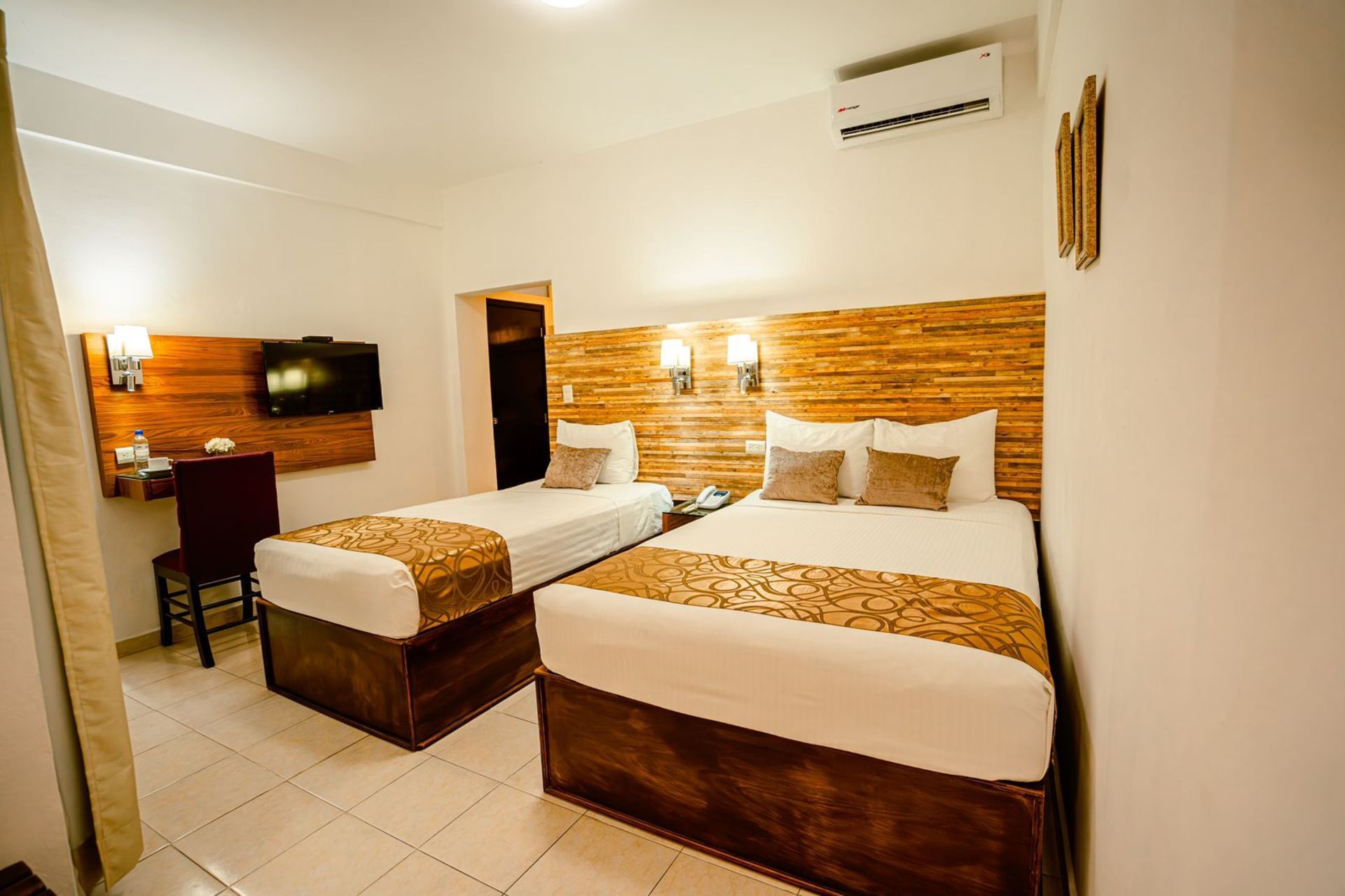 Habitación de hotel con dos camas individuales, cabeceros de madera, escritorio y TV.