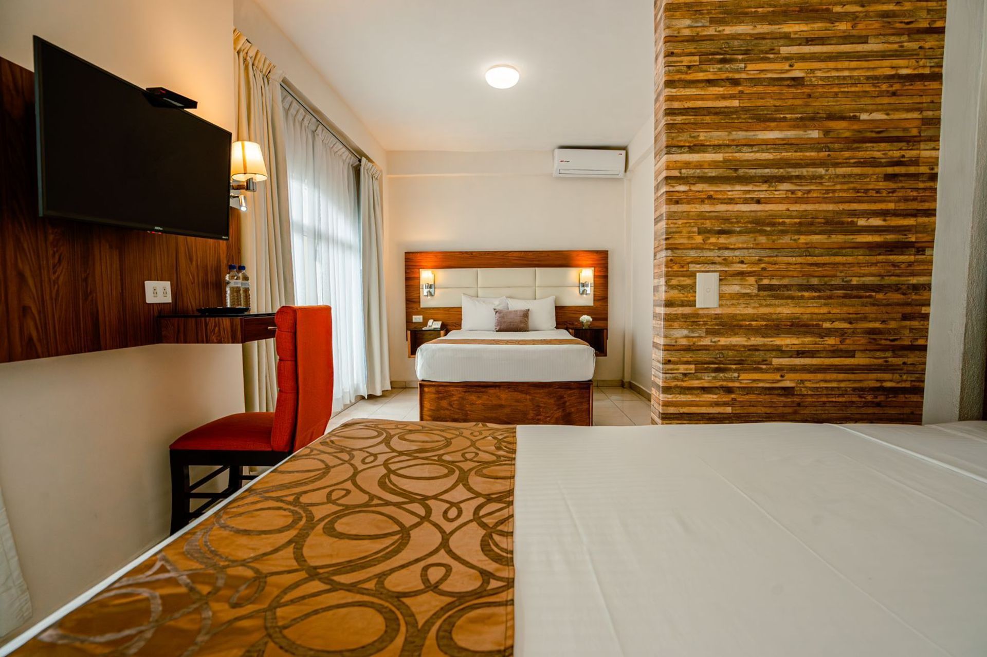 Habitación de hotel con cama, TV, silla roja y una pared decorativa de madera.