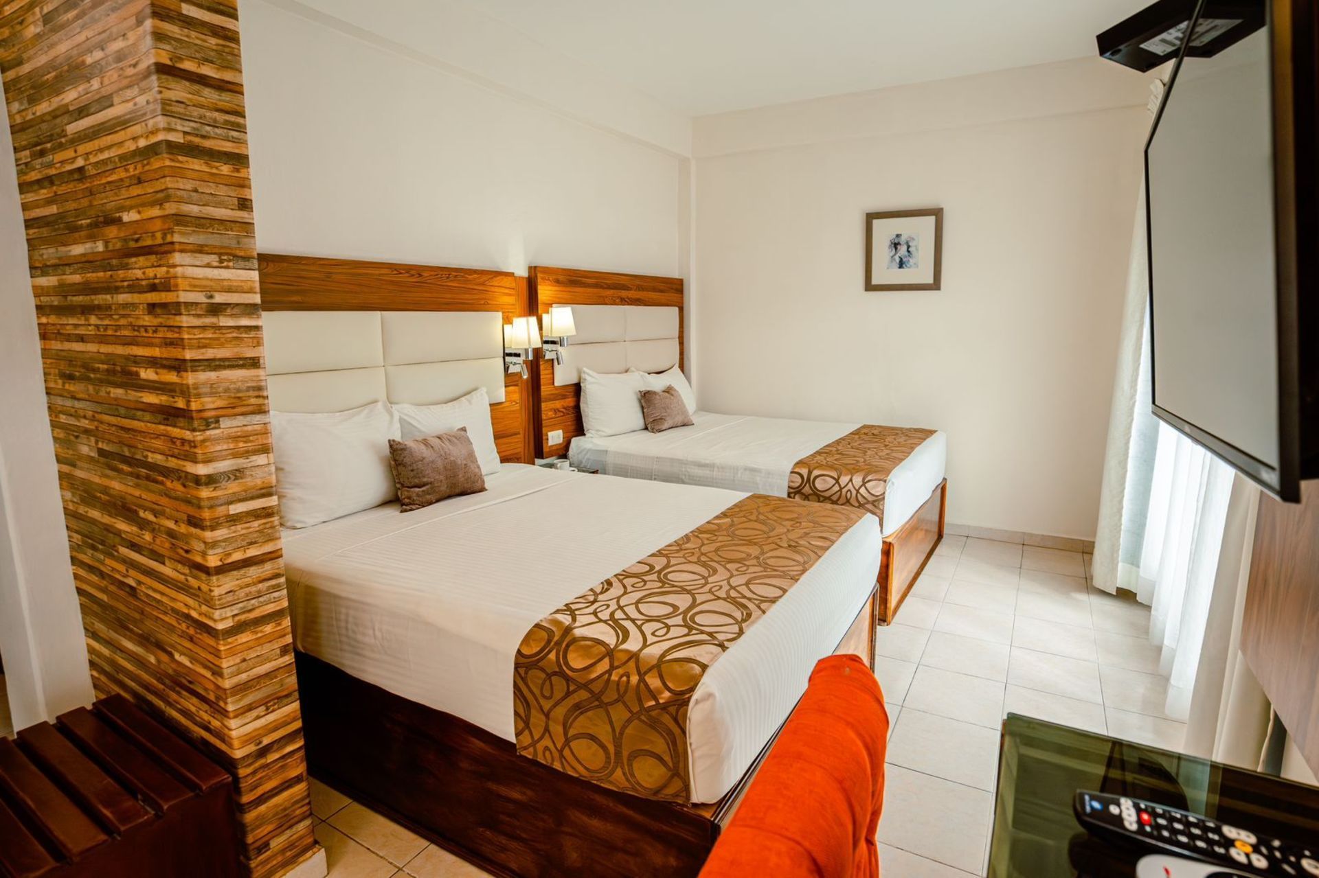 Habitación de hotel con dos camas, TV y una columna de ladrillo decorativa.