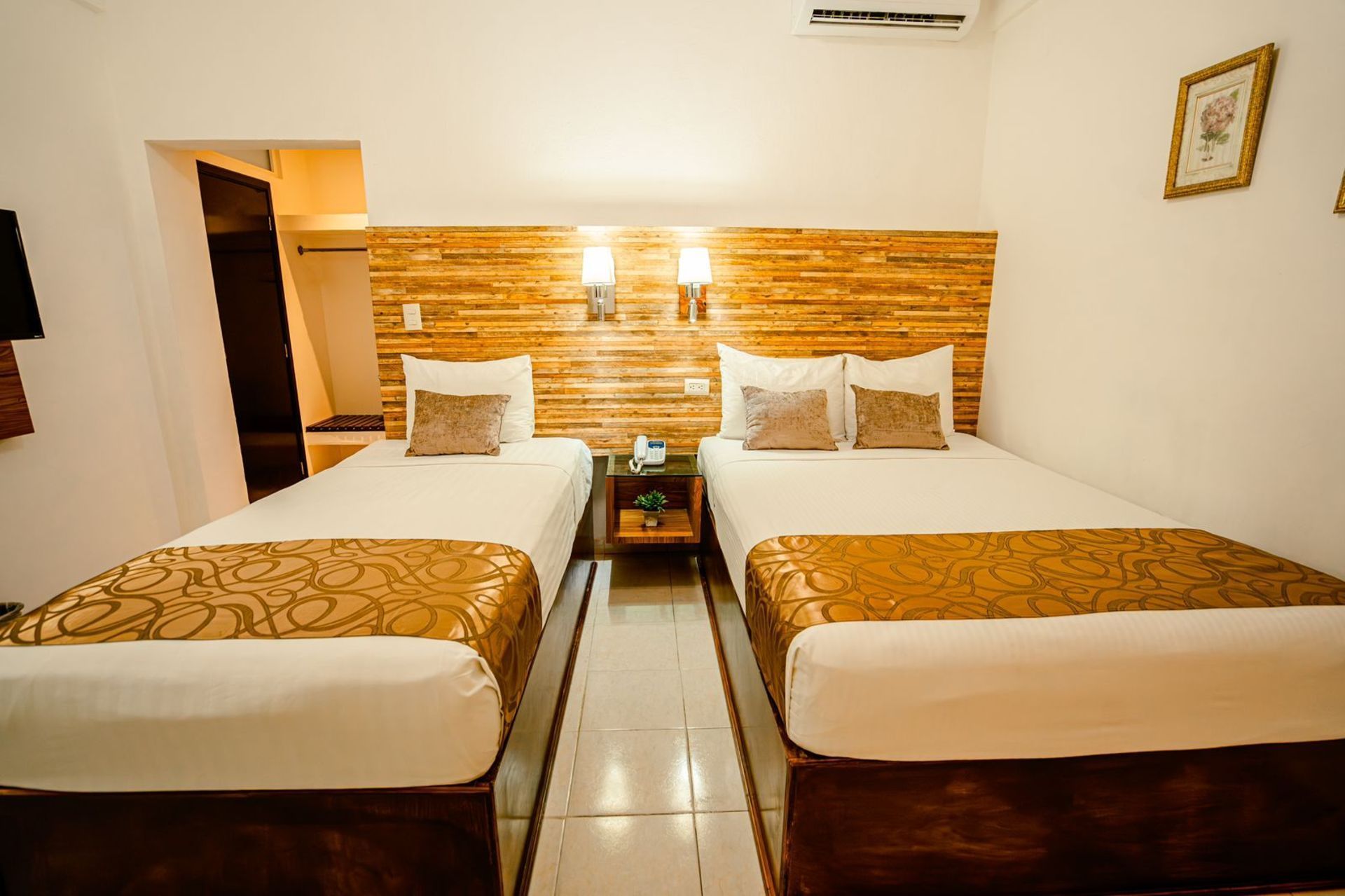 Dos camas individuales en una habitación de hotel, con cabecera de madera, almohadas decorativas y una mesita de noche.