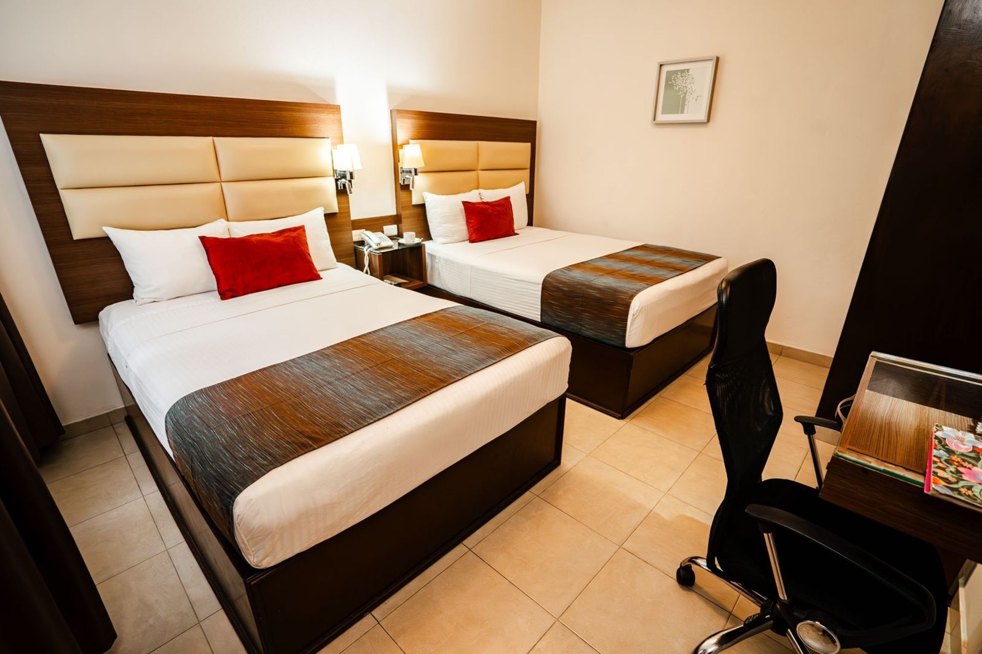 Dos camas individuales en una habitación de hotel, cada una con una almohada roja y una manta marrón y gris. 