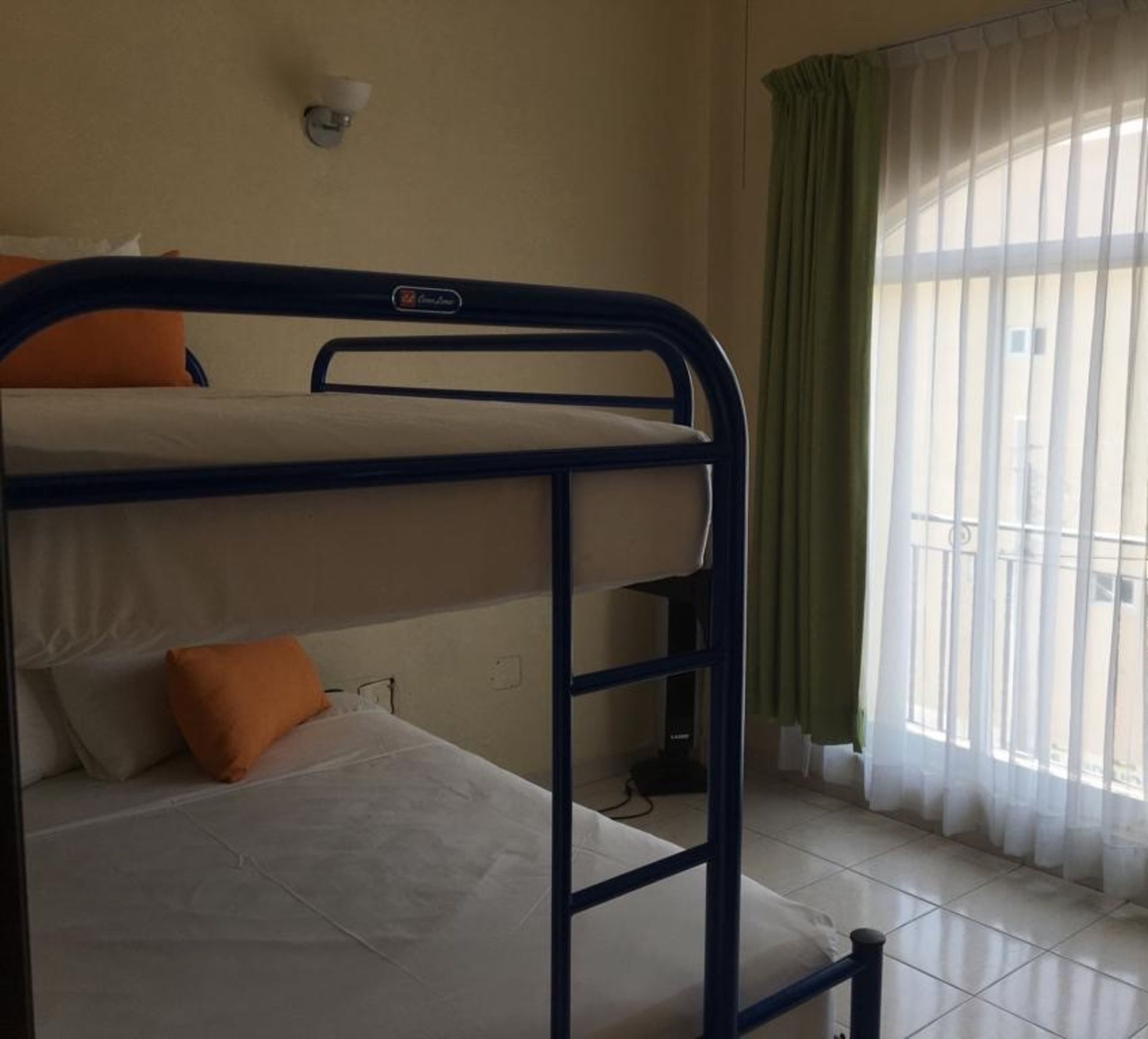 Literas en una habitación, con almohadas naranjas y una ventana con cortinas.