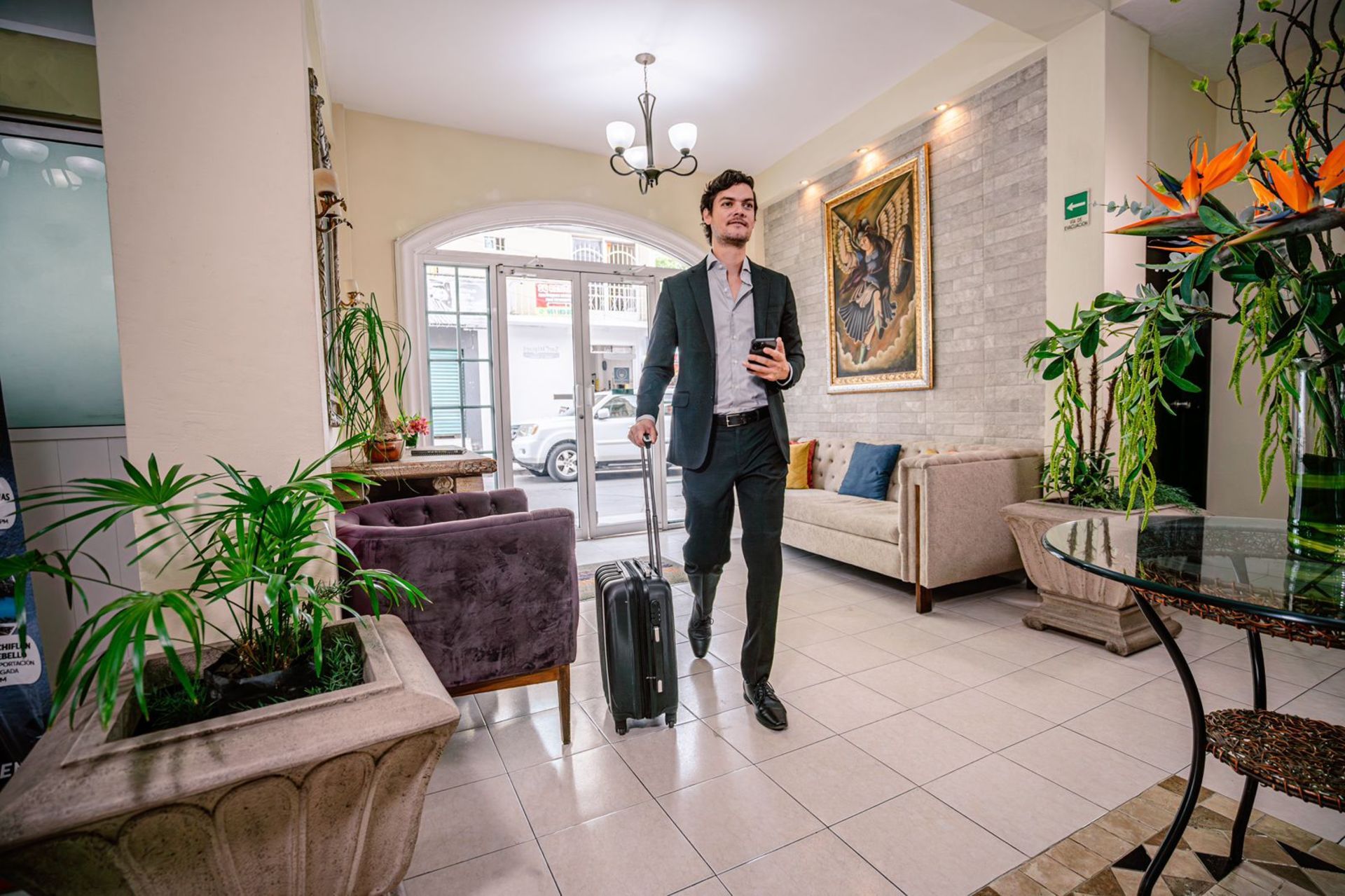 Un hombre de traje con equipaje camina por el vestíbulo del hotel, sosteniendo un teléfono.