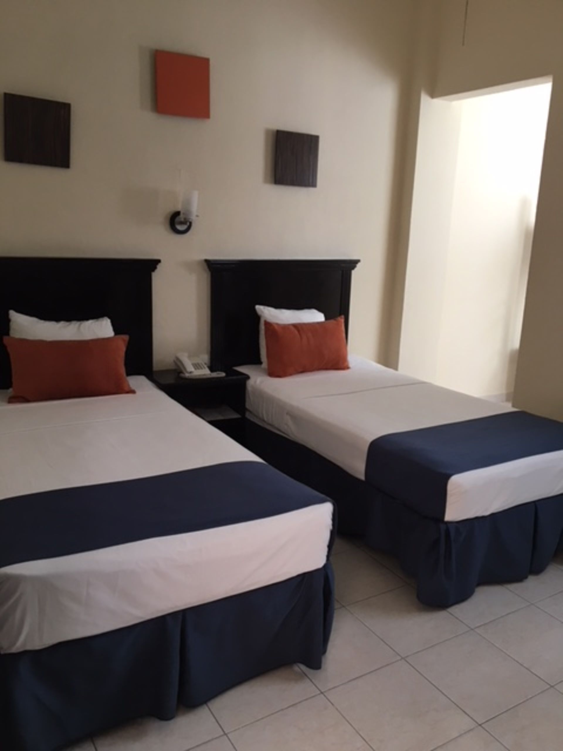 Dos camas individuales en una habitación de hotel, sábanas blancas, faldones de cama azul marino y almohadas naranjas