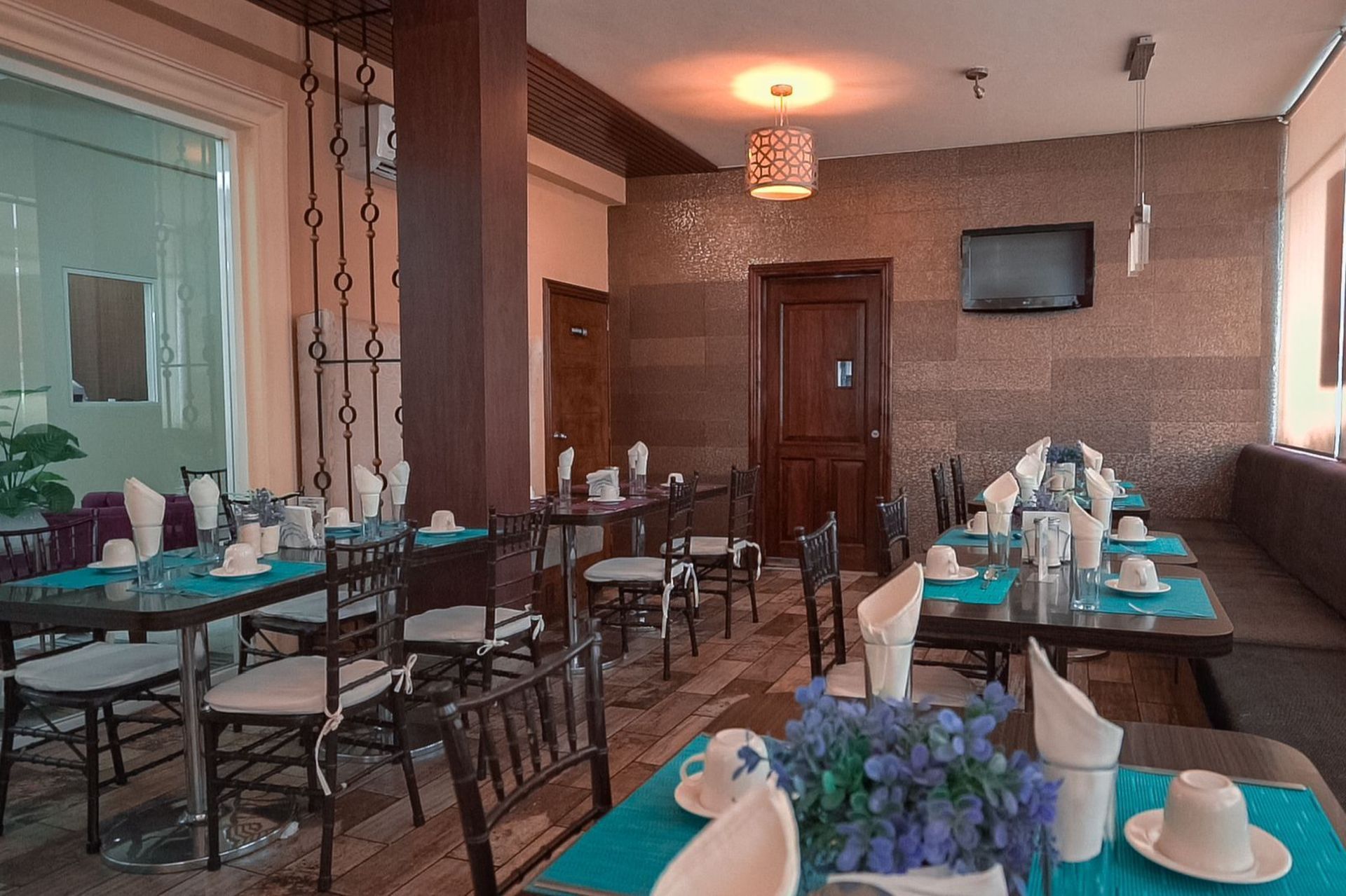 Interior de restaurante con mesas preparadas para cenar, manteles color verde azulado y tonos neutros.