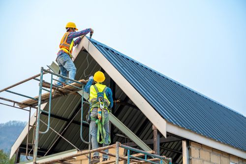 Two Construction Workers Are Working On The Blue Roof Of A Residential House - Millville, CA - Concrete Construction Excavating Inc.