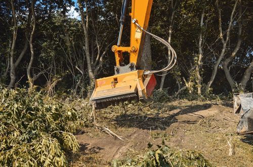 A Yellow Excavator Is Cutting Down Trees In A Forest - Millville, CA - Concrete Construction Excavating Inc.