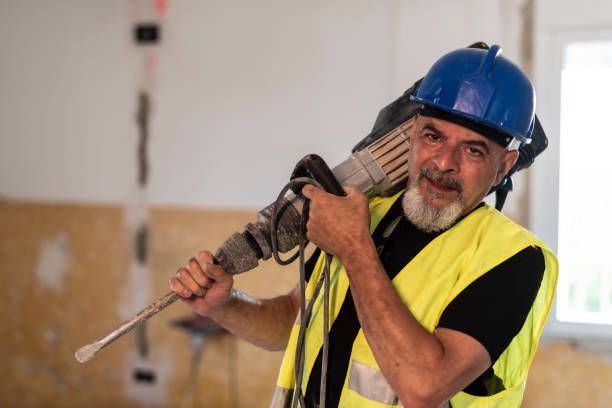 A Man Wearing A Hard Hat And Safety Vest Is Holding A Hammer Drill - Millville, CA - Concrete Construction Excavating Inc.