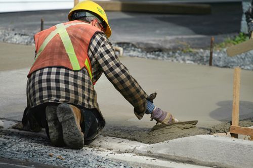 A Construction Worker Is Kneeling Down And Spreading Concrete With A Trowel - Millville, CA - Concrete Construction Excavating Inc.