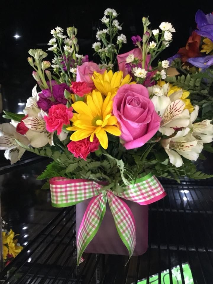 A purple vase filled with colorful flowers with a pink and green checkered bow