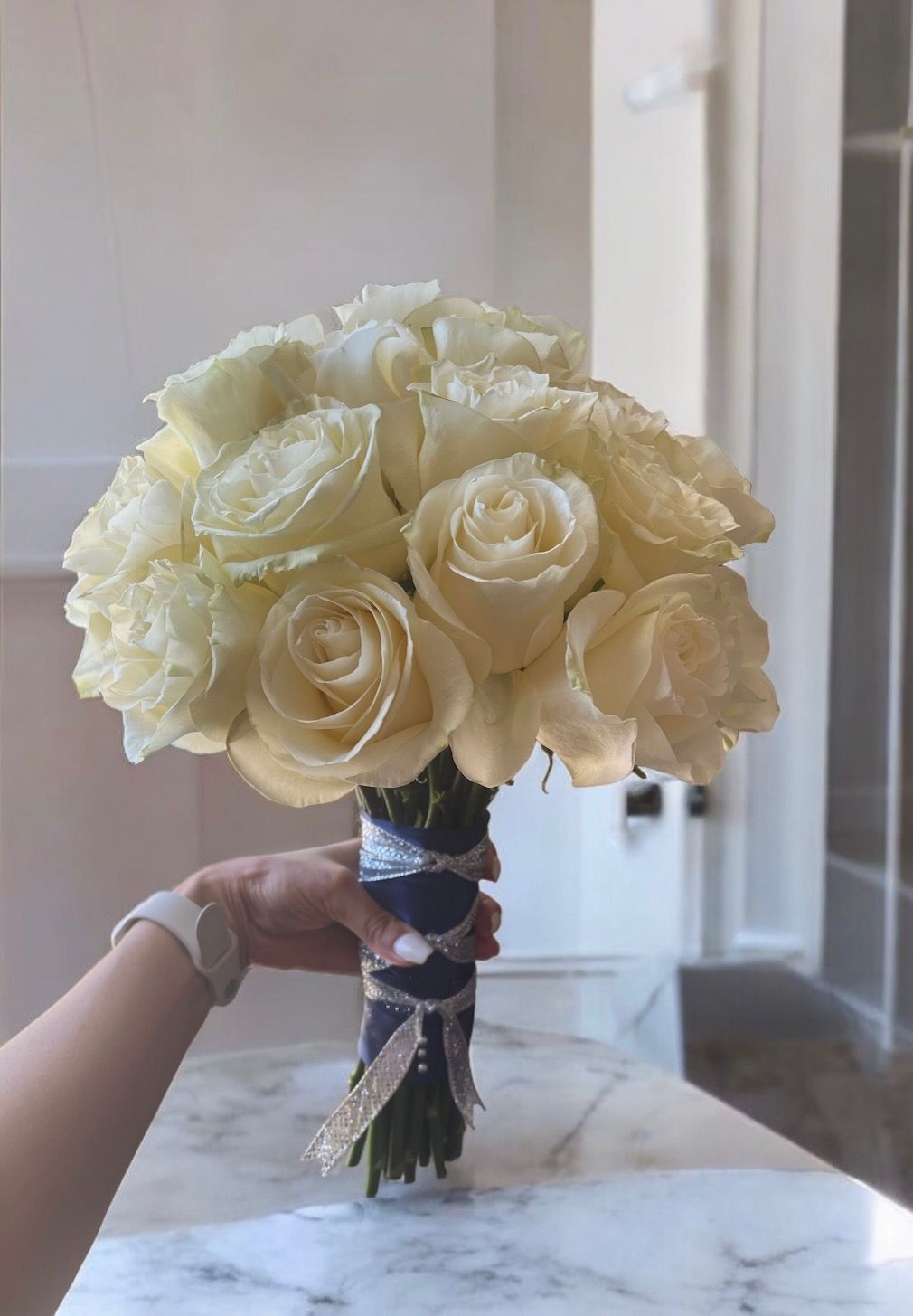 A person is holding a bouquet of white roses on a table.