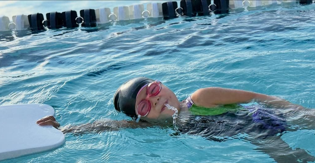 A woman is swimming in a pool wearing a yellow swim cap and goggles.