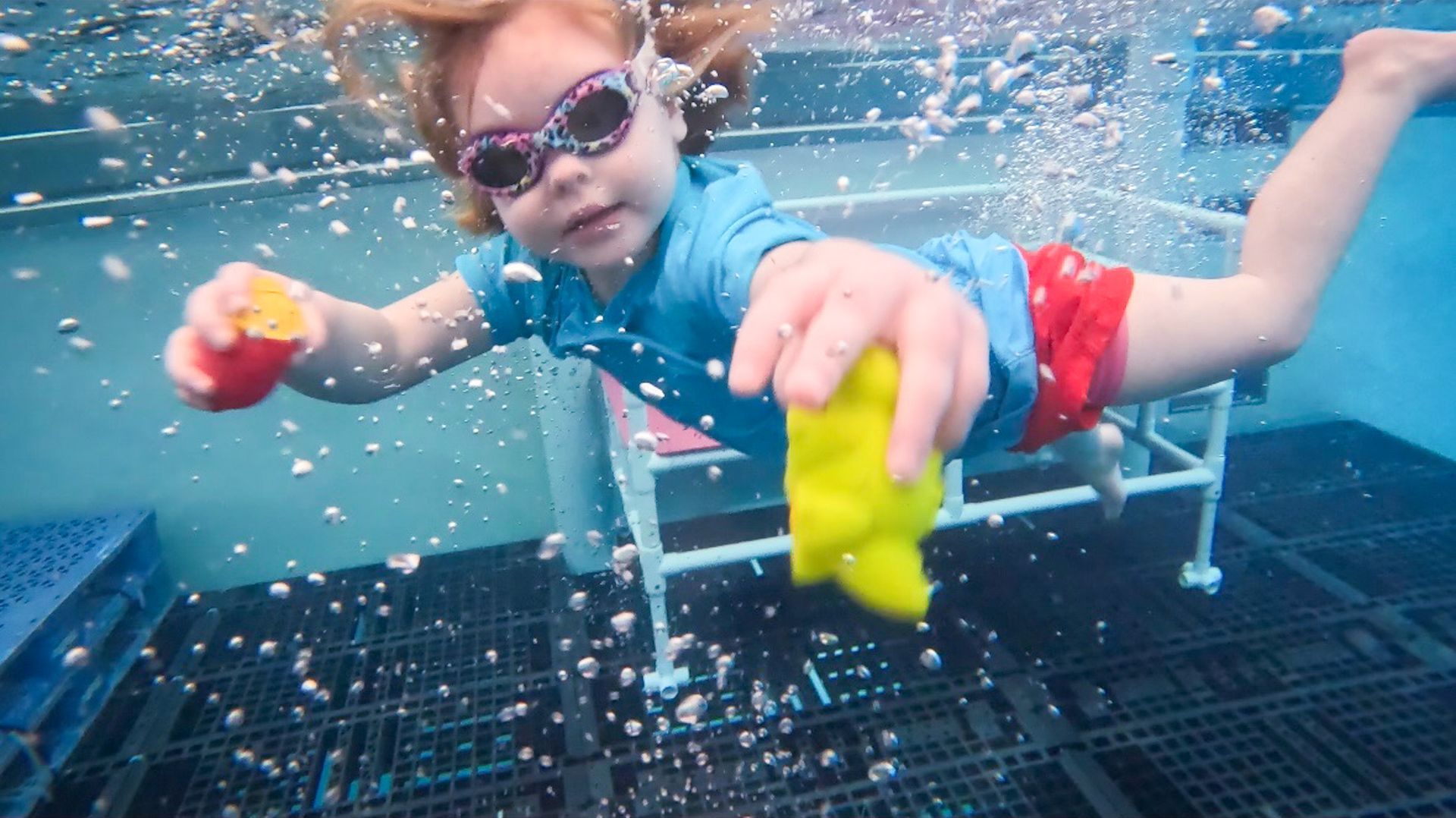 Two little girls wearing sunglasses are swimming in a pool.