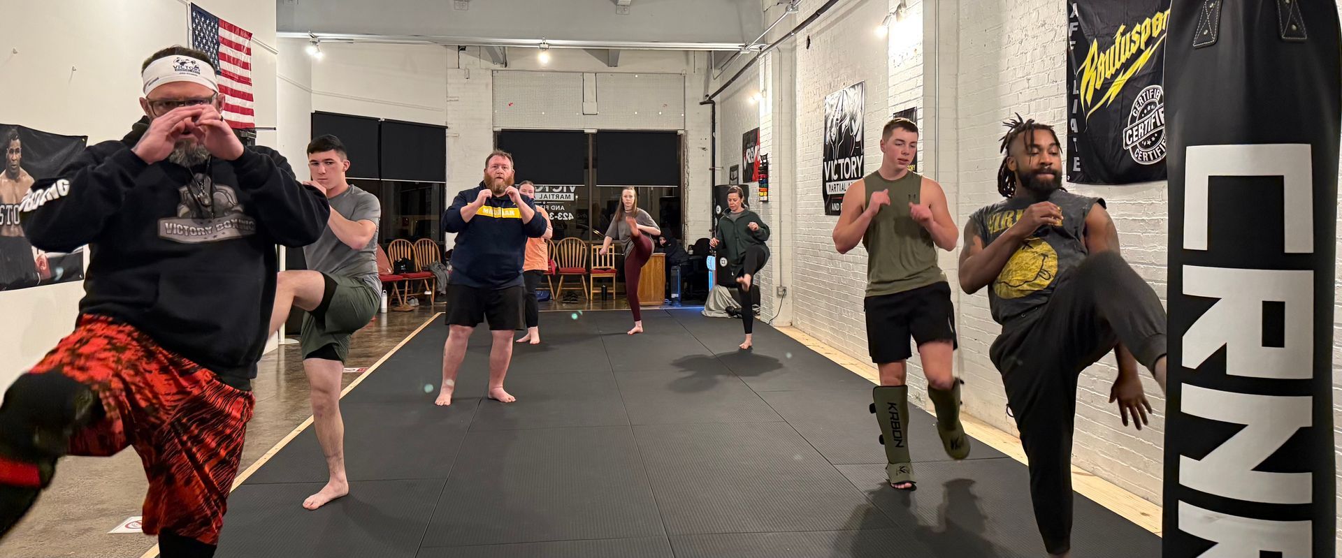 Two karate practitioners in white uniforms spar in a bright, white room. 